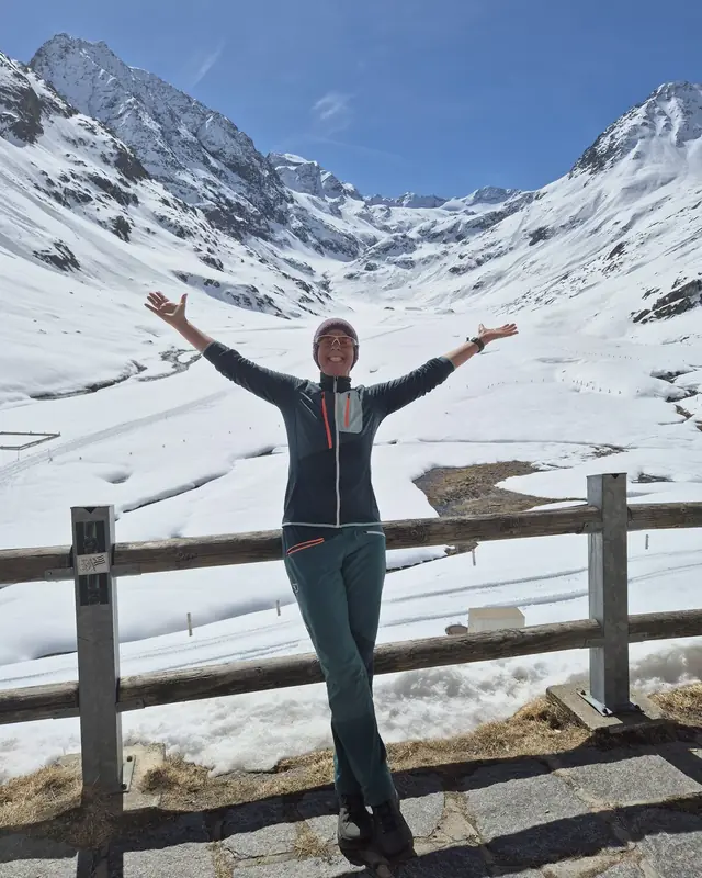Christina steht am Morgen vor verschneiten Alpengipfeln und breitet die Arme aus