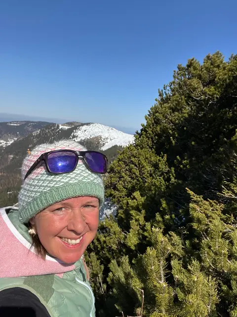 Selfie von Christina mit Mütze und Sonnenbrille vor verschneiten Bergen