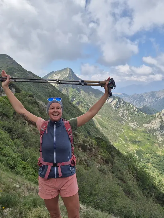 Christina reckt auf einem grünen Bergrücken die Wanderstöcke in die Höhe
