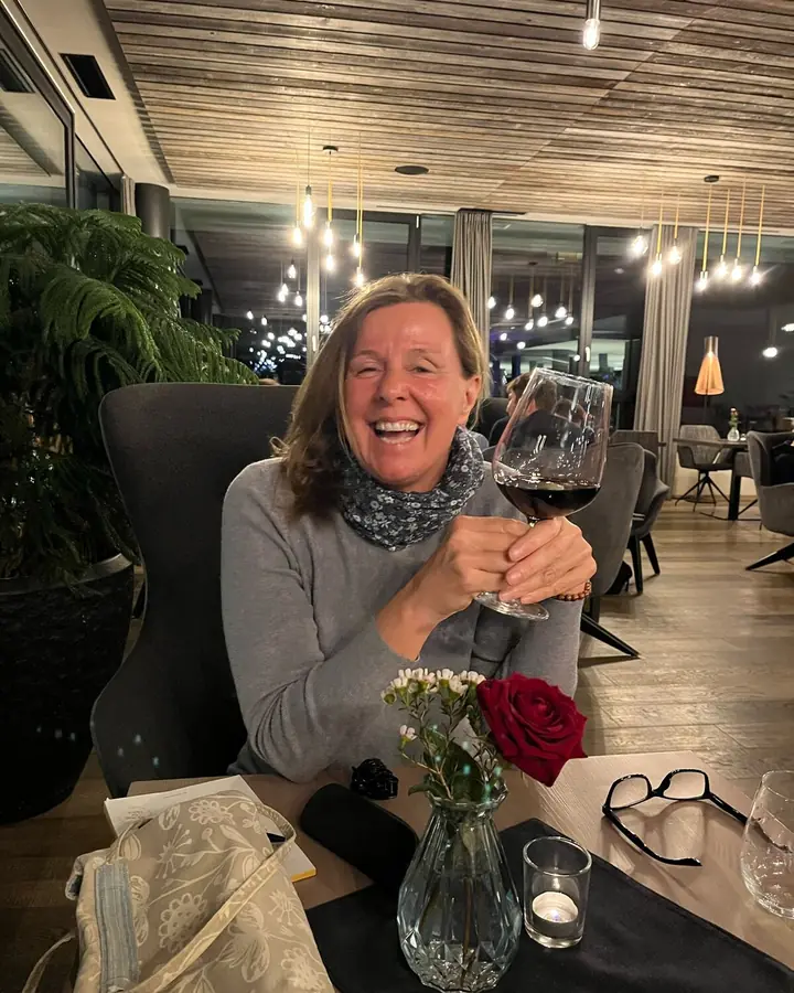 Christina sitzt lachend mit einem Glas Rotwein im Restaurant eines Hotels